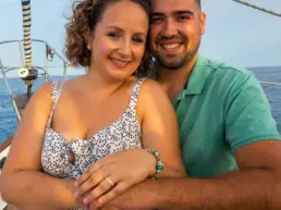 Young couple embracing and smiling on the bow of a sailing yacht, sea and sky behind them