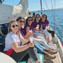Grupo de mujeres con camisetas moradas a juego sentadas en la cubierta del velero con bebidas