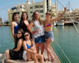Grupo de mujeres en bañador posando en la cubierta de un velero con Puerto Marina de Benalmádena al fondo