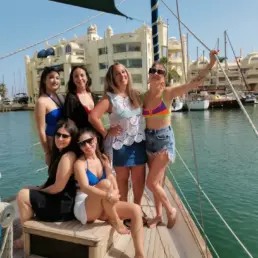 Grupo de mujeres en bañador posando en la cubierta de un velero con Puerto Marina de Benalmádena al fondo