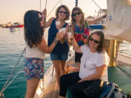 Four women toasting with glasses on a yacht's deck in warm afternoon light