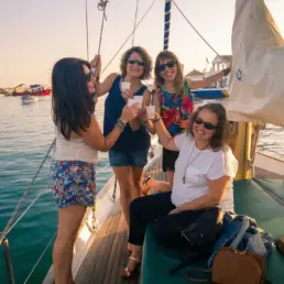 Four women toasting with glasses on a yacht's deck in warm afternoon light
