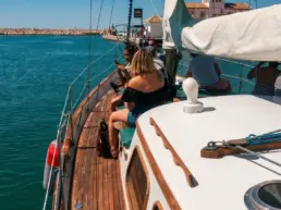 Passengers seated along a yacht's teak rail looking out to sea as it leaves the harbour