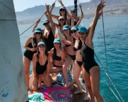Grupo de unas diez mujeres con gorras azules y los brazos en alto celebrando en la cubierta del velero