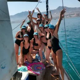 Group of around ten women in blue caps with arms raised celebrating on the yacht's deck