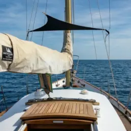 Vista desde la proa de un velero con la vela recogida hacia un mar en calma y cielo azul