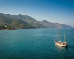Vista aérea panorámica de un velero navegando sobre agua turquesa junto a una costa montañosa verde
