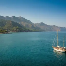 Panorama aérien d'un voilier naviguant sur une eau turquoise près d'une côte montagneuse verte