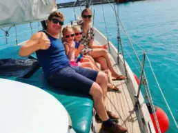 Family seated on a yacht's rail giving thumbs up over turquoise water with the breakwater behind