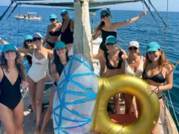 Group of women in blue caps on a yacht's deck with a green awning and golden float