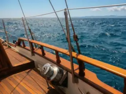 Close-up of a chrome winch and rigging on a yacht's teak rail with the open sea behind