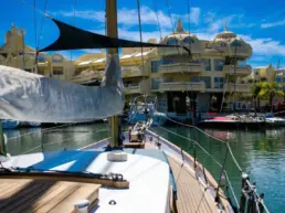 View from a yacht's bow towards Puerto Marina Benalmádena and its yellow building under blue sky