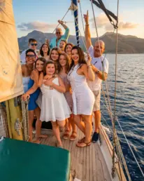 Grupo numeroso vestido de blanco celebrando con los brazos en alto en la cubierta de un velero