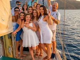 Large group dressed in white celebrating with arms raised on a yacht's deck