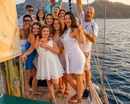 Grupo numeroso vestido de blanco celebrando con los brazos en alto en la cubierta de un velero