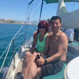 Pareja madura abrazada sentada en la cubierta de un velero sobre aguas turquesa