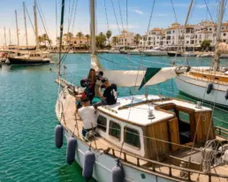 Passagers à bord d'un voilier amarré dans un port avec palmiers et immeubles blancs