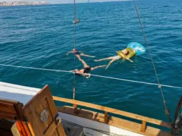 Three people floating beside a yacht, one on an inflatable lilo, seen from the deck