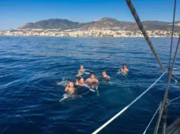 Five men swimming in the sea beside a yacht with the Benalmádena coast behind