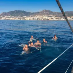 Five men swimming in the sea beside a yacht with the Benalmádena coast behind