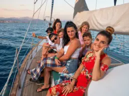 Family group posing smiling on a yacht's deck in the golden hour with the coast behind