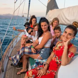 Family group posing smiling on a yacht's deck in the golden hour with the coast behind