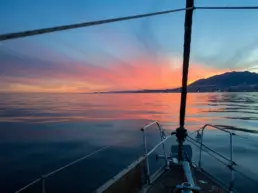Pink and violet sunset mirrored on a calm sea seen from a yacht's bow