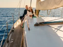Bride and groom embracing on a yacht's teak rail out at sea at sunset