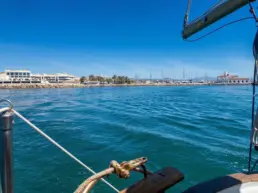 View from a yacht's bow leaving through the harbour mouth with a lighthouse and white buildings