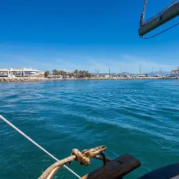 View from a yacht's bow leaving through the harbour mouth with a lighthouse and white buildings