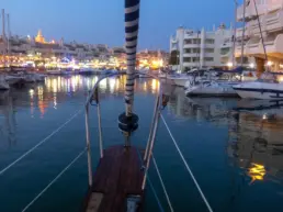 Benalmádena harbour at nightfall with the port lights mirrored on the water, seen from the bow