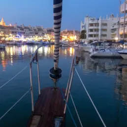 Dársena de Benalmádena al anochecer con las luces del puerto reflejadas en el agua, desde la proa